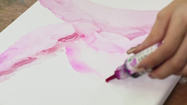 Close up of female artist paints an abstract picture, he uses pink paint fron tube on wet canves