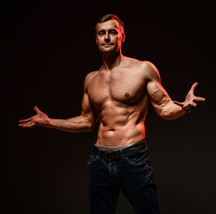 Handsome sexy man with muscular body, showing a welcome gesture, standing on a black background. Sports, bodybuilding motivation. Dark studio shot with copy space portrait