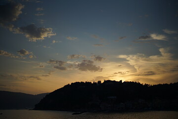 Romantic and wonderful sunset on an Italian beach. Silhouette of a hill under a summer sky at dusk. Sea, clouds and setting sun.