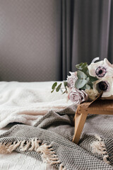 Coffee table on bed. Lilac roses, eucalyptus and anemones. Interior gray tones