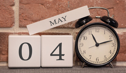 Important date, May 4, spring season. Calendar made of wood on a background of a brick wall. Retro alarm clock as a time management concept.