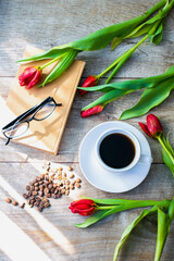 Cup of coffee espresso and beans, bouquet of red tulips. book. womens mothers day spring concept