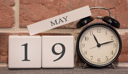 Important date, May 19, spring season. Calendar made of wood on a background of a brick wall. Retro alarm clock as a time management concept.