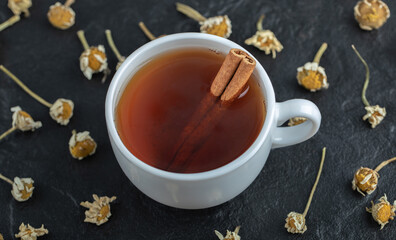 Obraz na płótnie Canvas Cup of tea with cinnamon and pile of dried chamomiles