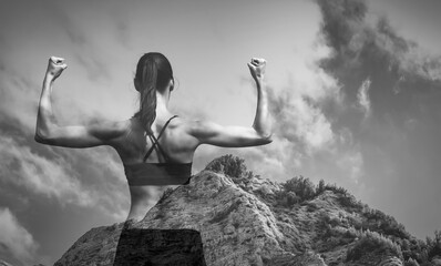 Strong young female flexing her arms against mountain background 