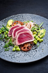 Modern style traditional Japanese gourmet seared tuna fish steak tataki with soba noodles and stir-fried vegetables served as close-up on a Nordic design plate with copy space