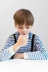 Caucasian boy sits at a white table and drinks clean water from a plastic cup. A child sits in a cafe