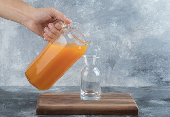 Male hand pouring orange juice into glass