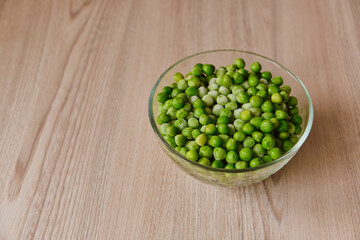 Frozen green peas in a glass plate stands on a wooden kitchen