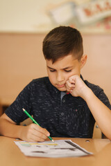 Naklejka na ściany i meble Concentrated schoolboy sitting at desk and writing in exercise book. Learning concept