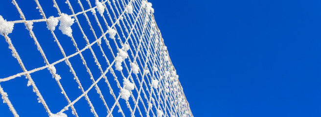 Volleyball net covered with snow against blue sky on clear winter day. Nature's minimalism. Banner format.
