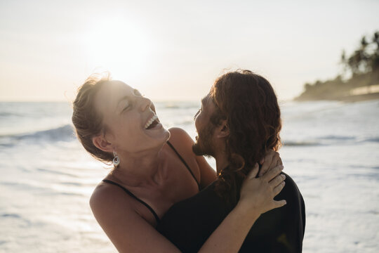 Amid the ocean waves, a man hugs a woman and they laugh cheerfully. High quality photo