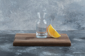 Slice of orange and empty glass on wooden board