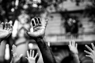 Multicultural hands raised in the air asking for freedom in a demonstration on street in black and white. Open palm of a black hand and white hands. Stop racism. Stop repression. - obrazy, fototapety, plakaty