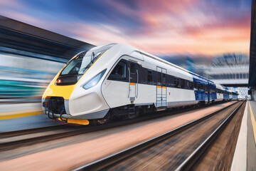 High speed train in motion on the railway station at sunset. Modern intercity passenger train with...
