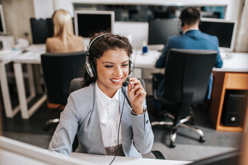 Beautiful smiling female call center worker accompanied by her team working in the office.