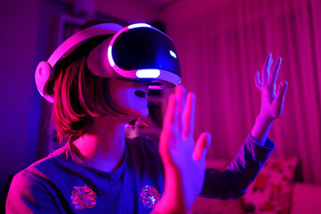 Pretty teenage girl wearing virtual reality headset in a dark room. Cute teen using VR glasses to...