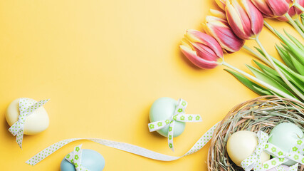 Easter eggs Colourful egg with tape ribbon, spring tulips, white feathers on pastel yellow background in Happy Easter decoration. Festive decoration in flat lay.
