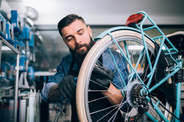 Young beard bicycle mechanic repairing bicycles in a workshop..