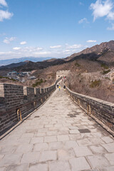 Fototapeta premium Beijing, China - April 28, 2010: Great Wall of China. Looking down on sloped walkway on top of wall which meanders over brown hills under blue cloudscape. Clothing adds bright colors.