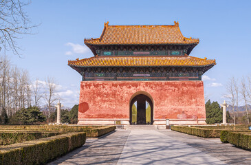 Beijing, China - April 28, 2010: Ming Tombs Changling. Double roofed entrance hall with giant Stele visible through opening under blue sky. Gray stone path leads to it in green garden.