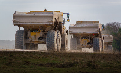 Three yellow Volvo A40E and A40F articulated dump truck earth movers in a convoy kicking up dust as they navigate across Salisbury Plain, Wiltshire UK