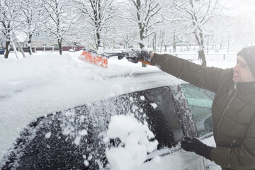 Removing snow from car with a brush. Man cleans his car after a snowstorm.