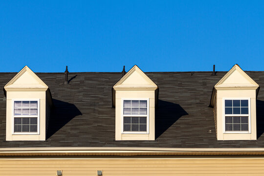 Close up isolated image of three false dormer windows (gabbled style) on a shingles covered roof at a modern house. These features are nonfunctional but have cosmetic and decorative purposes in USA.
