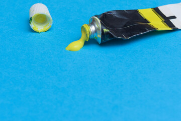 Tube of spilling yellow acrylic paint on art paper background