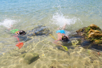 children practicing snorkeling with a colorful net on the shore of a crystal clear water beach
