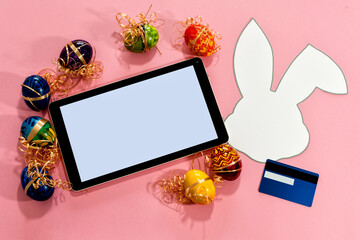Top view of tablet, easter eggs, paper rabbit and credit card.