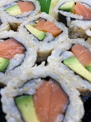 Takeout tray of salmon and avocado sushi rolls made with brown rice.