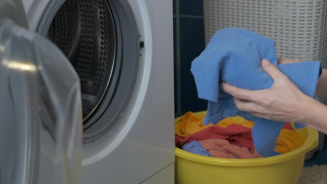 Woman load the clothes in washing machine. The female puts colored clothes in the washer.
