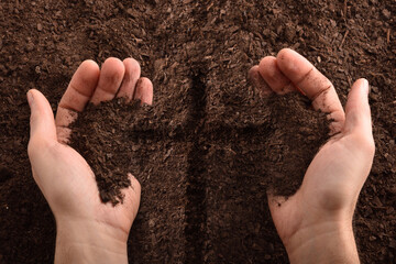 Hands with dirt and cross engraved on the dirt floor