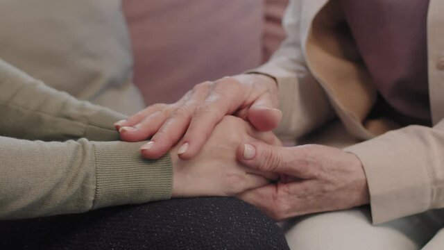 Slow-motion close up of unrecognizable women holding hands, supporting each other in difficult situation