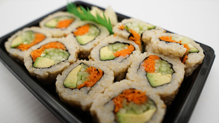 Takeout tray of vegetable sushi made with avocado, carrots, cucumber, and brown rice.