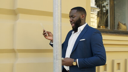 Smiling business man playing with cash on city street. Afro man walking outdoors
