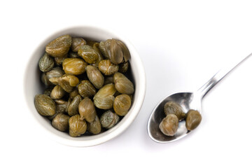 Top view of a bowl of green capers and a spoon isolated on a white background. 