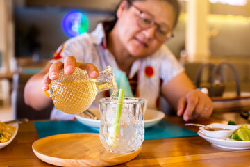 Selective focus to hand of Asian female customers pouring Lemongrass juice into a glass. The concept of a refreshing drink from nature.
