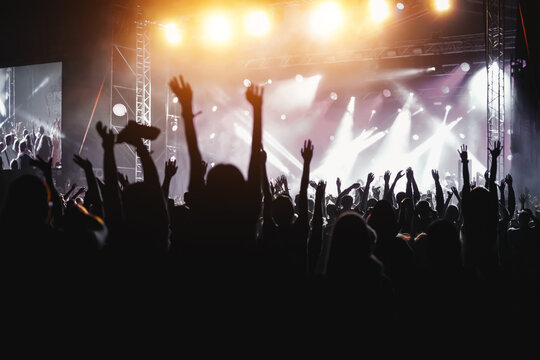 People with raised hands, silhouettes of concert crowd in front of bright stage lights.
