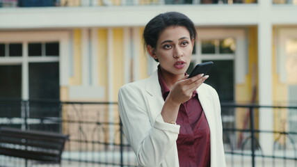 Fototapeta premium Focused mixed race woman making phone call outside. Lady talking on speakerphone