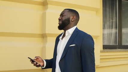 Fototapeta premium Upset afro businessman receiving bad message. Sad african guy walking outdoors