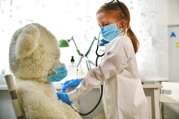 a girl plays a doctor, listens, makes a virus test and a vaccination for a teddy bear