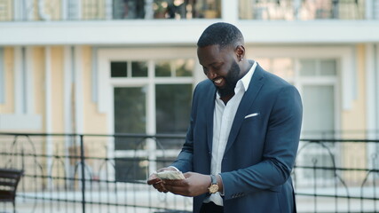 Cheerful african businessman holding dollars outdoors. Afro guy keeping money