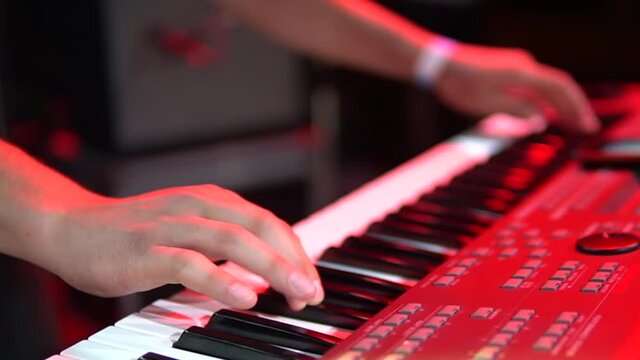 plays a synthesizer at a night concert close up, hands beating the keys