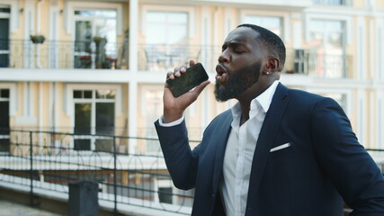 Happy african businessman dancing with phone outdoors. Winner afro man dancing