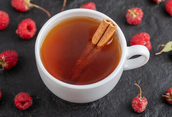 Cup of tea and fresh raspberries on black background