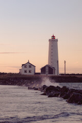 Wave crushes stones near the lighthouse during the sunset in Iceland