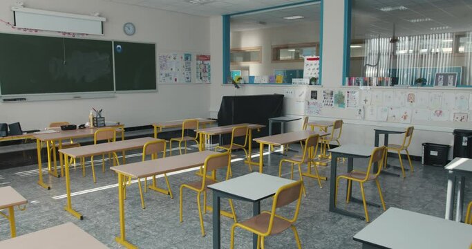 Empty classroom with chairs and desks with a chalkboard and drawings on the wall. Class without pupils, with individual school desks. Inside view of a schoolroom in primary or lower secondary school.