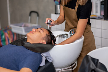 Close up hands inject water to wash Asian man hair after finish process of haircare in beauty salon shop.
